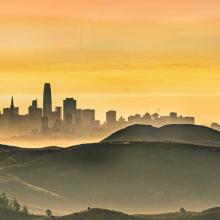 Skyline of San Francisco including rolling hills and fog.
